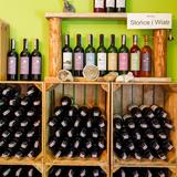Zdjęcie przedstawia produkty winiarskie z Winnicy Słońce i Wiatr. Na półkach stoją oraz leżakują butelki zawierające wina wszelkiego rodzaju oraz koloru.