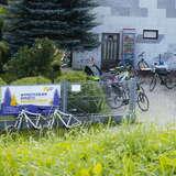 Baner reklamujący wypożyczalnie zawieszony na ogrodzeniu, za ogrodzeniem ustawionych kilka rowerów dla klientów